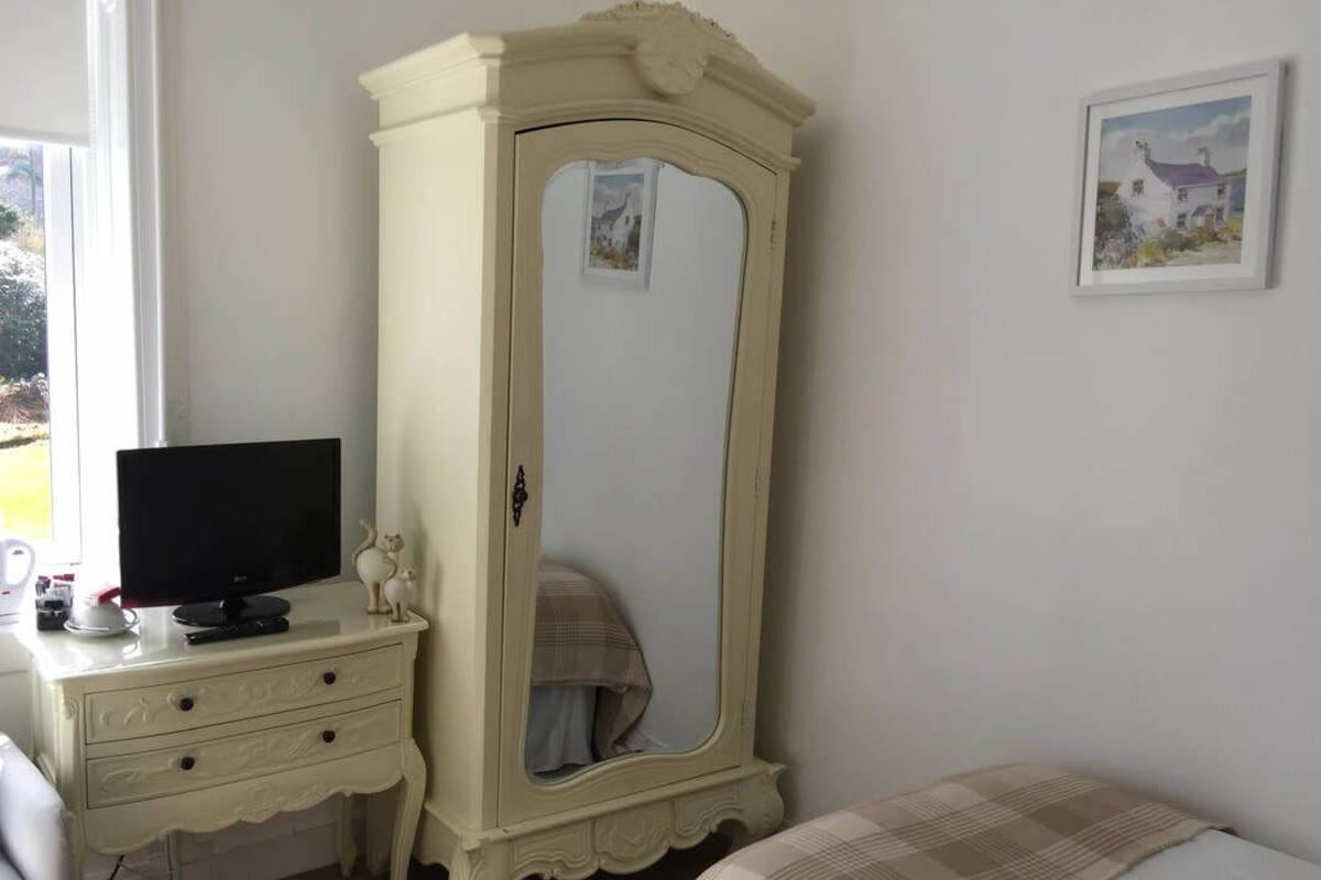 A bedroom with a white wardrobe, a bed with a plaid blanket, a television on a nightstand, and a framed picture on the wall.