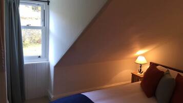 Un dormitorio con una cama, una mesita de noche con lámpara, una ventana con cortinas y vistas al exterior.