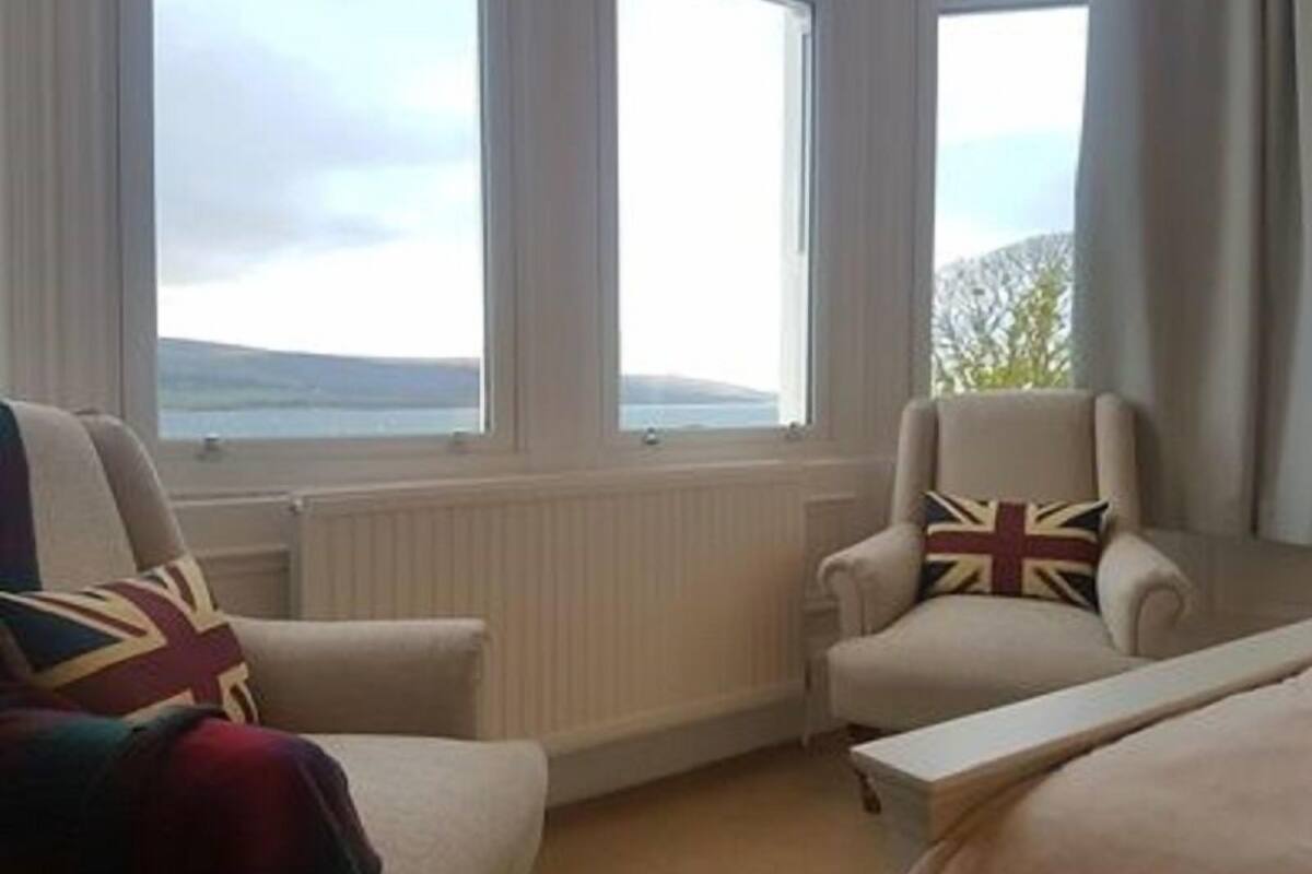 A room with two armchairs and a bed, large windows with a view of the sea, and a radiator under the windows.