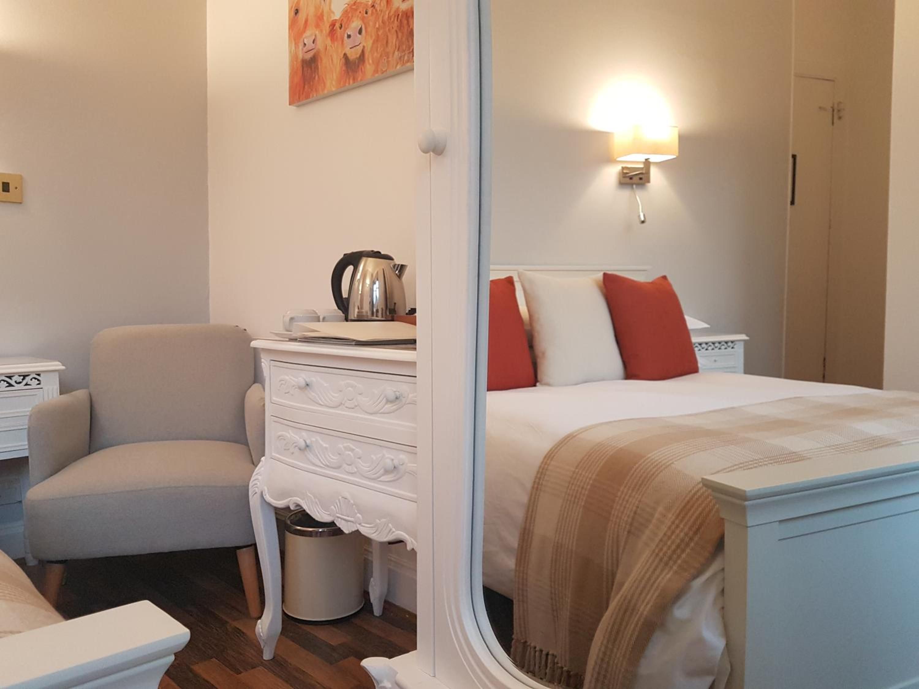 A bedroom with a bed, a chair, a dresser, a nightstand, and a wall-mounted lamp.