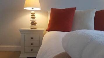 A bedroom with a bed, white bedding, a nightstand with a lamp, and a stack of stones.