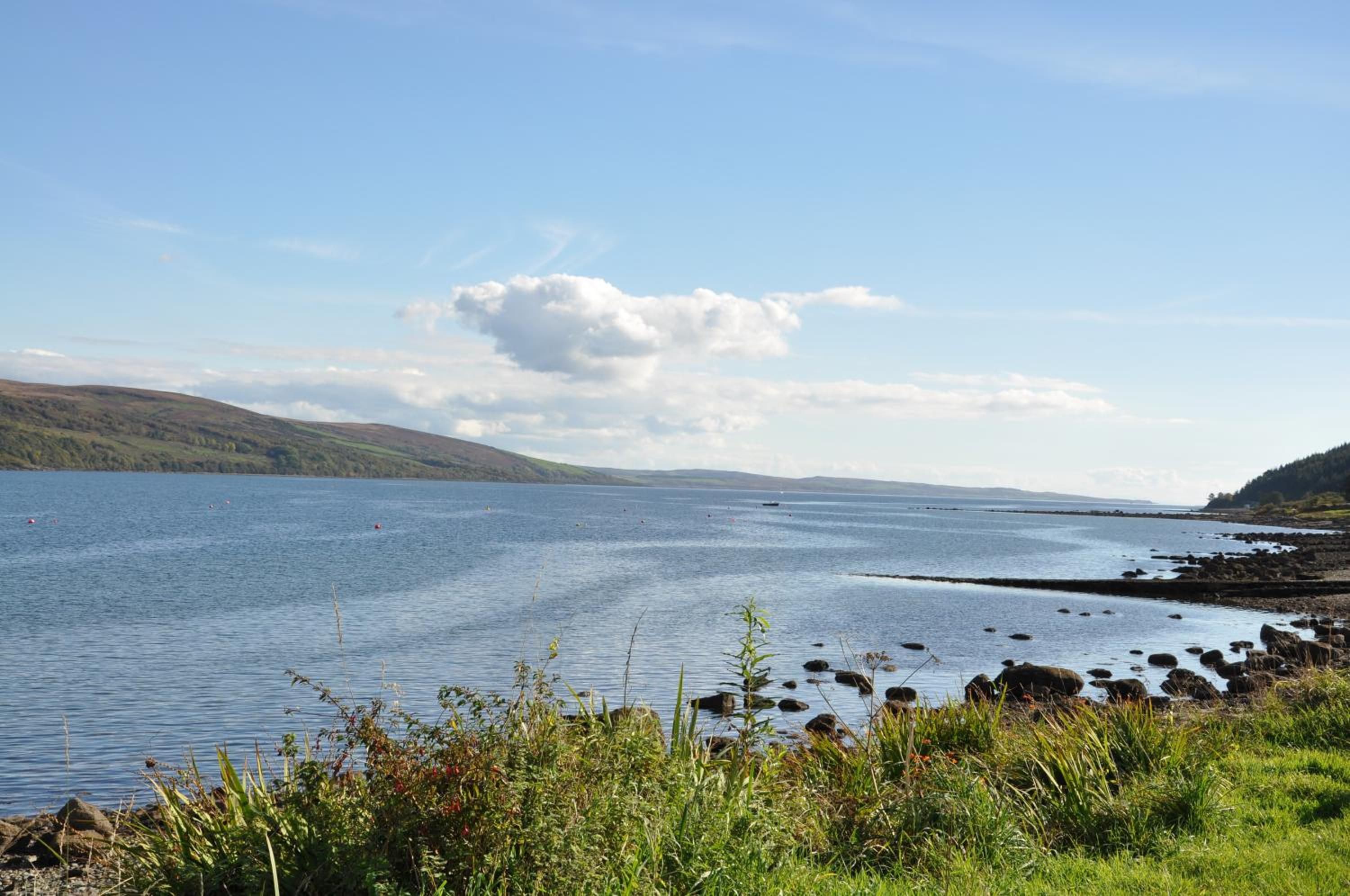 A calm lake with a rocky shoreline and distant hills.