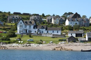 A coastal hotel with a prominent sign, multiple buildings, and a beach in the foreground. - Kames Hotel (Tighnabruaich)