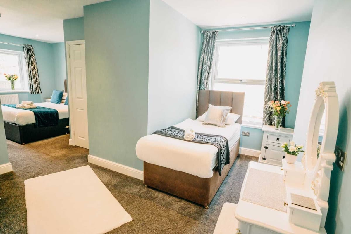 A bedroom with a bed, a bedside table, a dresser, a window with curtains, and a mirror.