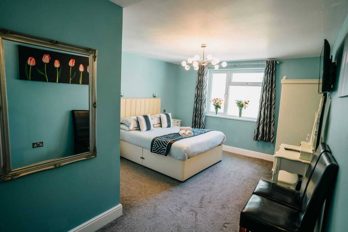 A bedroom with a bed, a mirror, a window with curtains, and a chandelier.