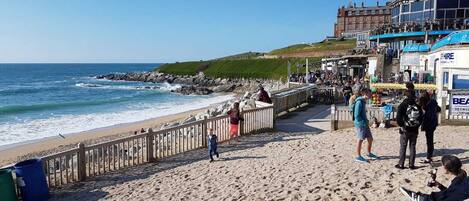 A beach with a wooden walkway, a building with 'The Stable' sign, and a 'Hire' sign.