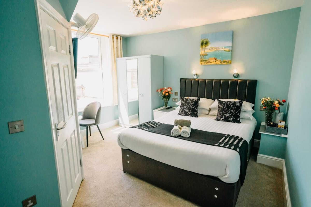 A bedroom with a bed, bedside tables, a chair, a desk, and a painting on the wall.