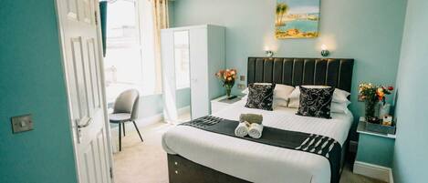 A bedroom with a bed, bedside tables, a chair, a desk, and a painting on the wall.