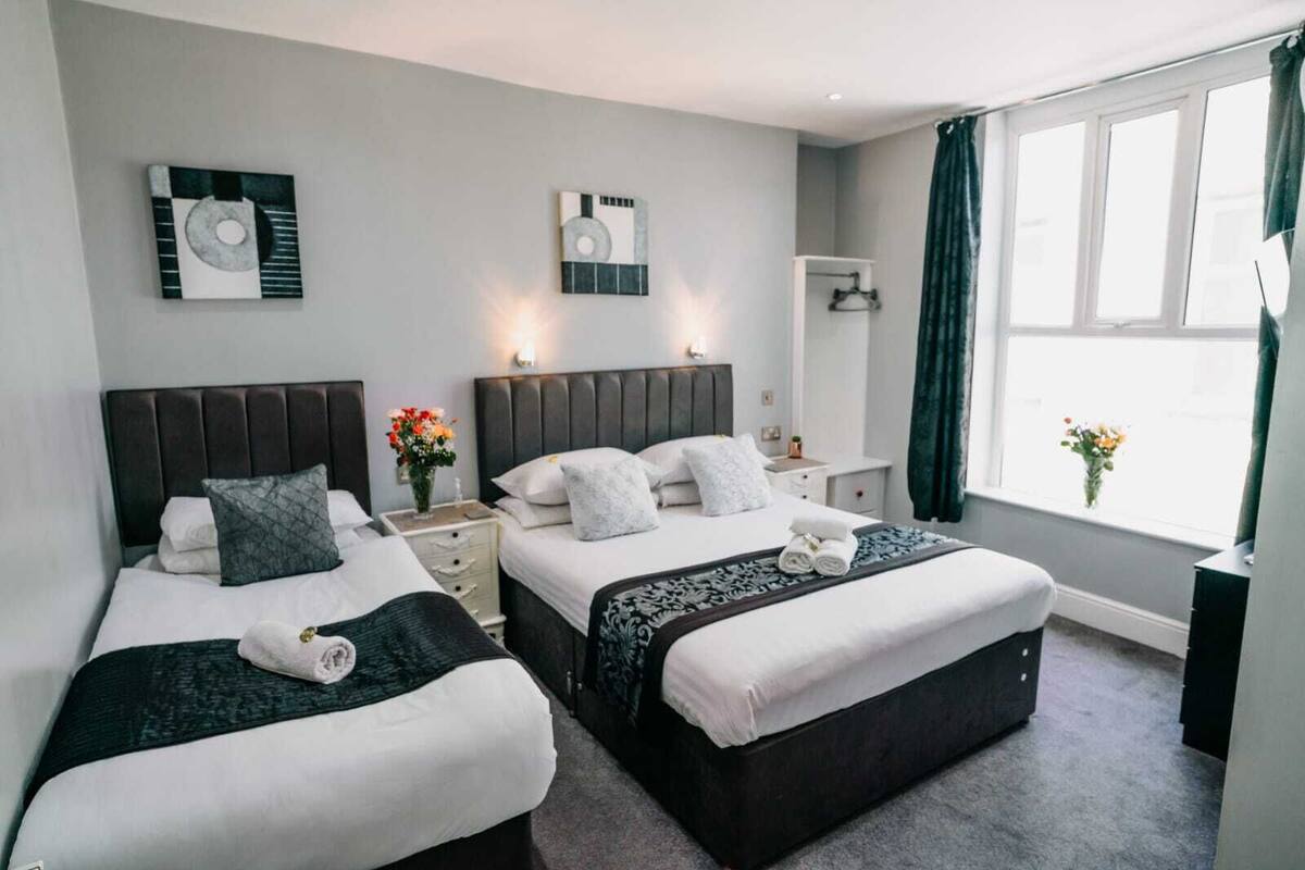 A hotel room with two beds, a large window with curtains, and artwork on the walls.