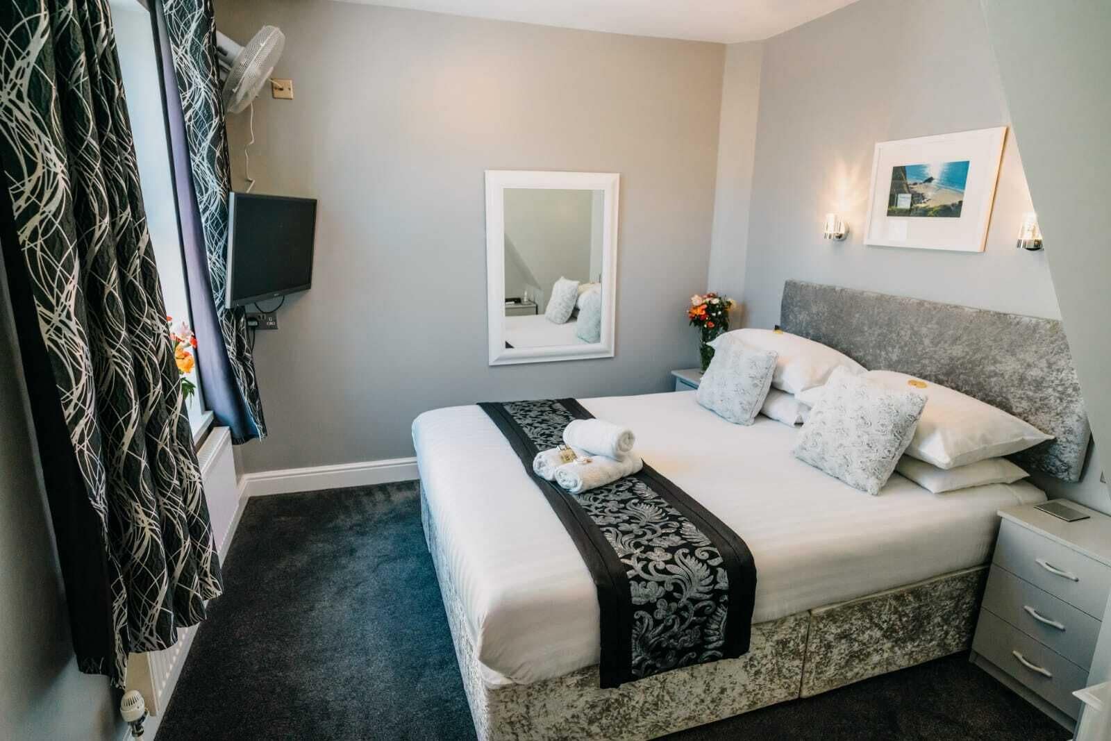A neatly arranged bedroom with a bed, bedside tables, a mirror, and a wall-mounted TV.