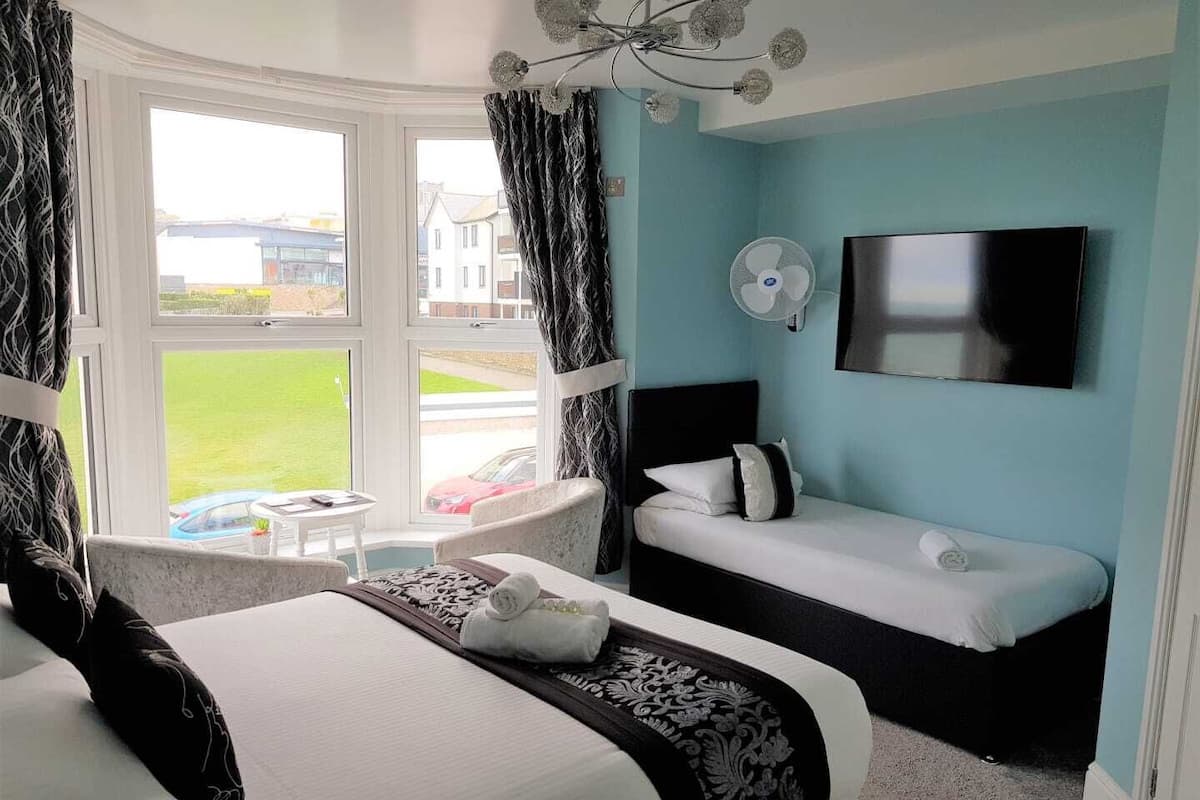 A hotel room with a bed, a sofa, a TV, and a window with curtains.