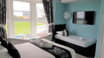 A hotel room with a bed, a sofa, a TV, and a window with curtains.