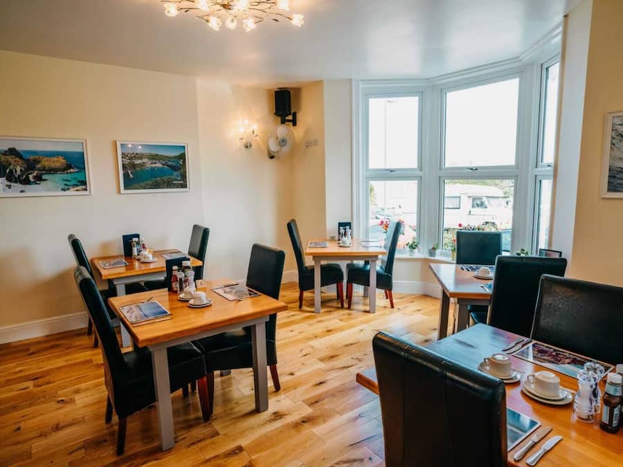 A dining area with wooden tables and black chairs, framed pictures on the walls, and large windows.