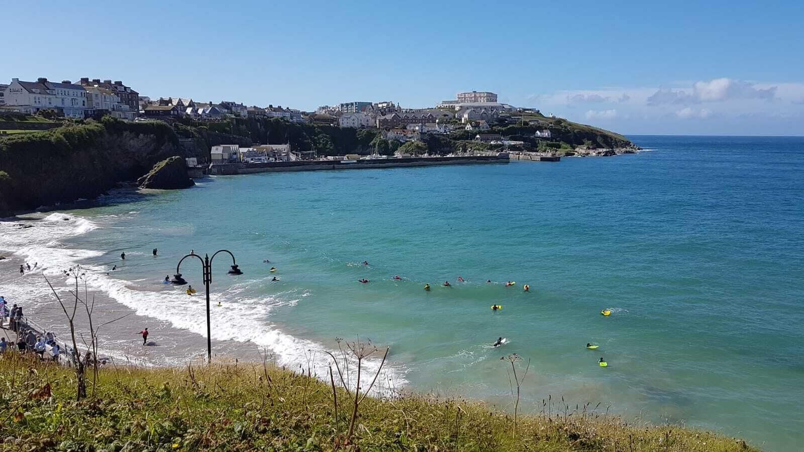 A coastal town with a beach, a lighthouse, and buildings on a hill.