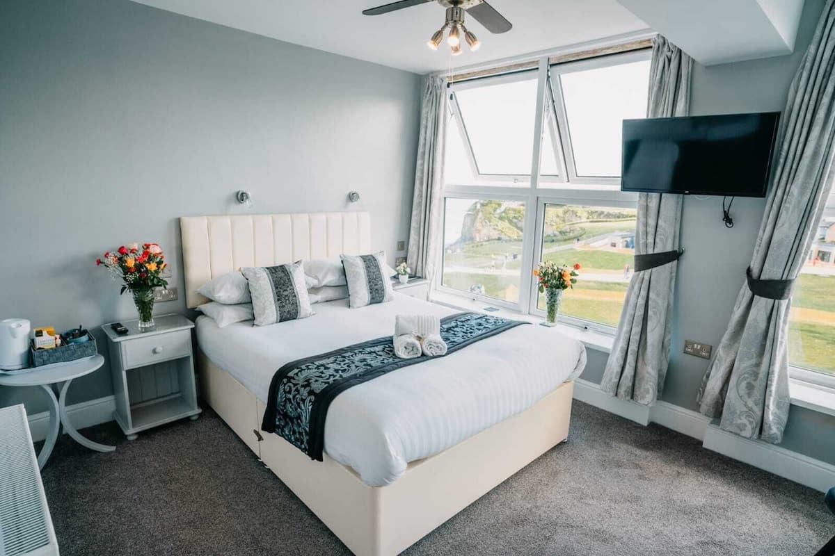 A modern hotel room with a large bed, a TV mounted on the wall, and a view of the outdoors through the window.