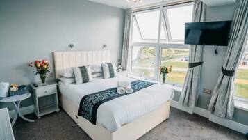Habitación de hotel moderna con una cama grande, un televisor montado en la pared y vistas al exterior a través de la ventana.