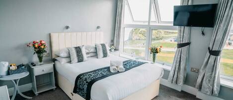 A modern hotel room with a large bed, a TV mounted on the wall, and a view of the outdoors through the window.