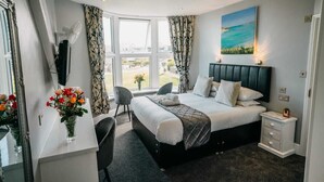 Une chambre d’hôtel moderne dotée d’un grand lit, d’un bureau, d’une chaise et offrant une vue sur la ville grâce à de grandes fenêtres.
