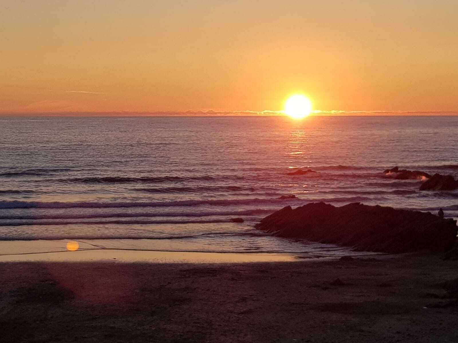 A sunset over a beach with waves and rocks.