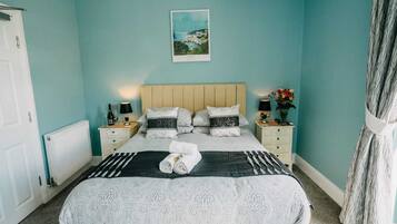 A bedroom with a bed, two bedside tables, a nightstand, a radiator, a picture on the wall, and a curtain.