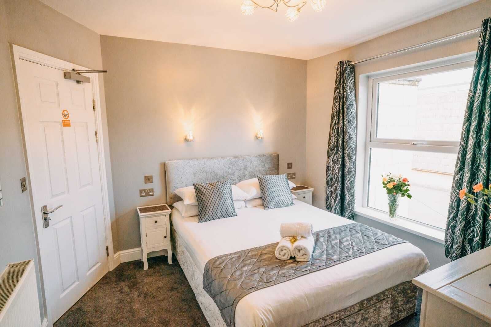 A hotel room with a bed, bedside tables, a window with curtains, and a view of the outside.
