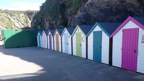 Une rangée de cabanes de plage aux couleurs vives, avec une falaise rocheuse en arrière-plan.