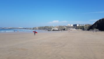 Una extensa playa arenosa con cielo azul despejado, algunas personas y edificios al fondo.