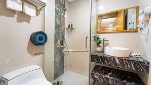 A bathroom with a glass-enclosed shower, a white toilet, a marble sink, and a mirror with a wooden frame. - The Blue Hotel (Ho Chi Minh City)