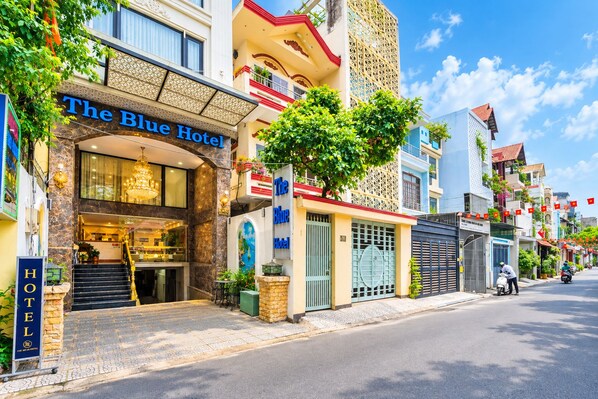 Un hotel con una entrada destacada, una escalera que lleva al vestíbulo y vista a la calle con scooters estacionados.
