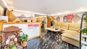 A hotel reception area with a reception desk, a sofa, and a coffee table. There are signs indicating check-in times and a no-smoking policy. - The Blue Hotel (Ho Chi Minh City)