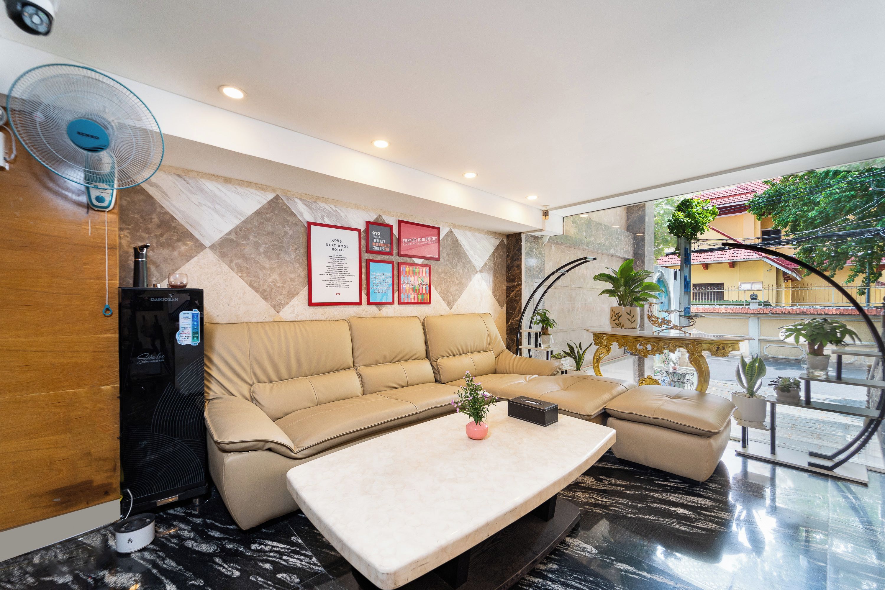 Un moderno vestíbulo de hotel con un sofá seccional color beige, una mesa de centro de mármol y un ventilador de pared.