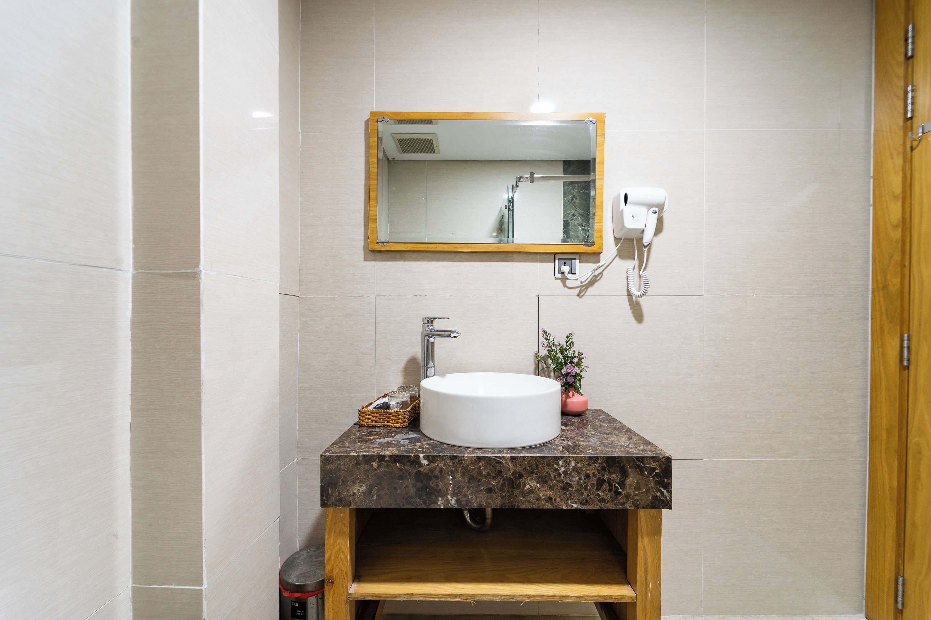 Une salle de bain avec un lavabo en marbre, un miroir, un sèche-cheveux et une petite plante en pot.
