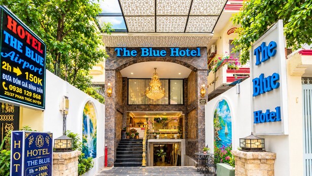The entrance to The Blue Hotel with a staircase leading to the lobby, a chandelier, and a mural of a sea scene. - The Blue Hotel (Ho Chi Minh City)