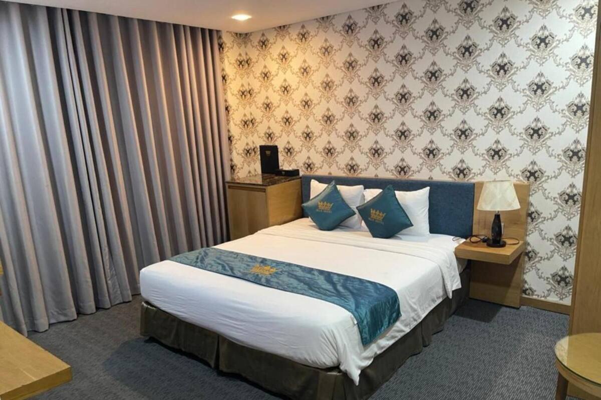 Une chambre d’hôtel avec un grand lit, une table de chevet, une lampe et une vue sur l’extérieur par la fenêtre.
