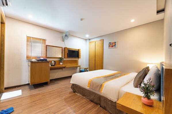 A hotel room with a bed, a desk, a television, a window with blinds, and a small painting on the wall.