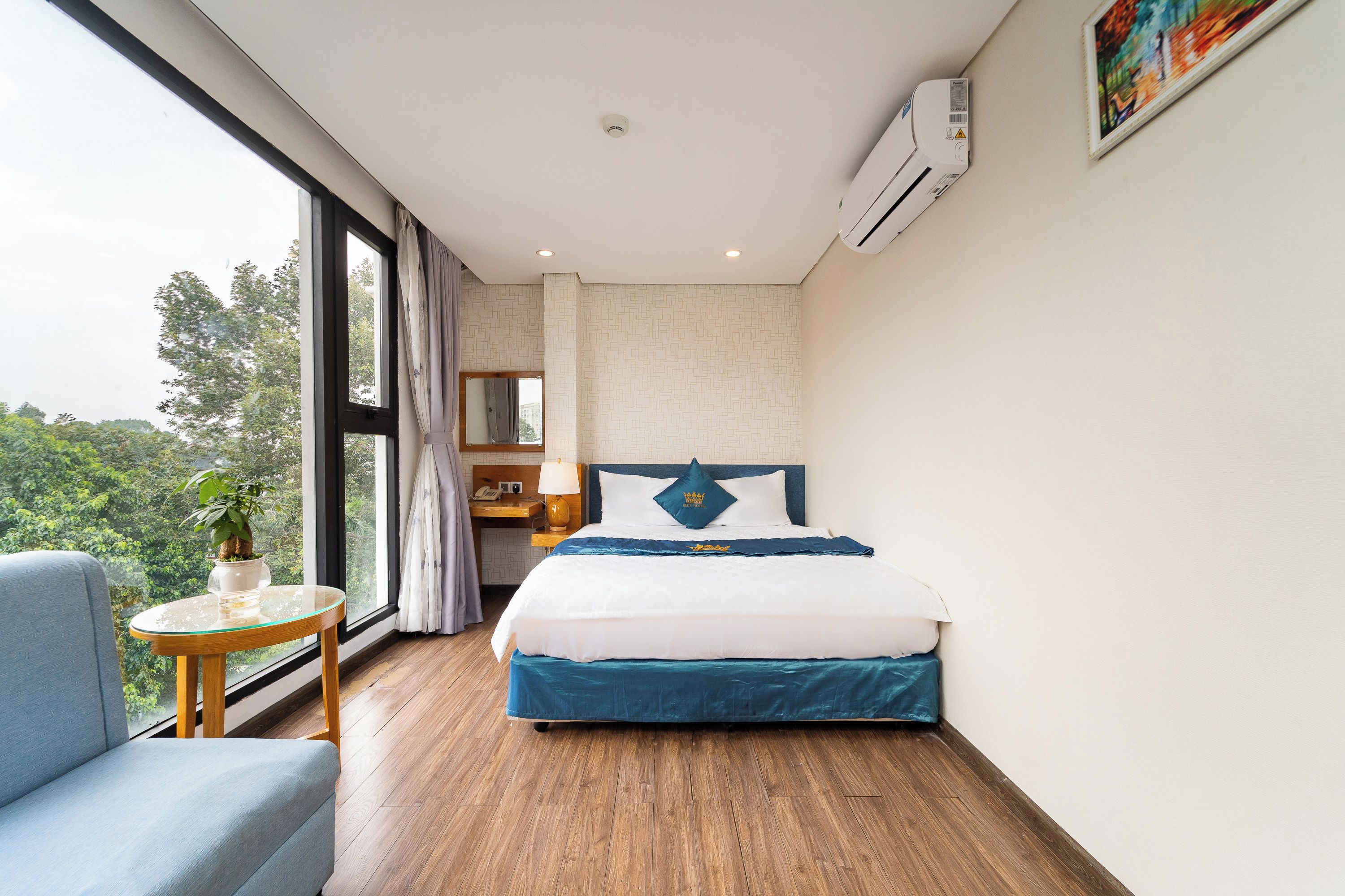 A hotel room with a bed, a desk, a chair, a window, and an air conditioning unit.
