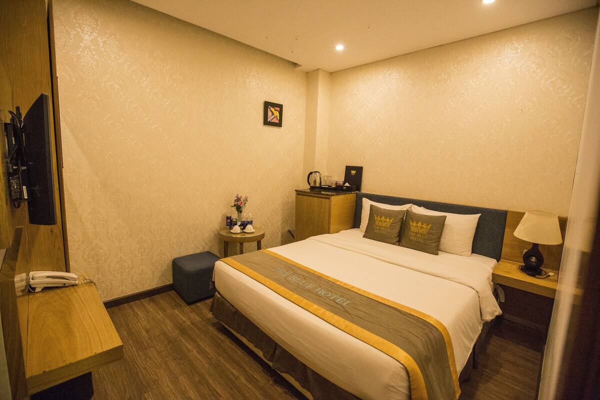 Une chambre d’hôtel avec un grand lit, une table de chevet avec une lampe, une petite table d’appoint avec un vase et un téléviseur posé sur un meuble en bois.