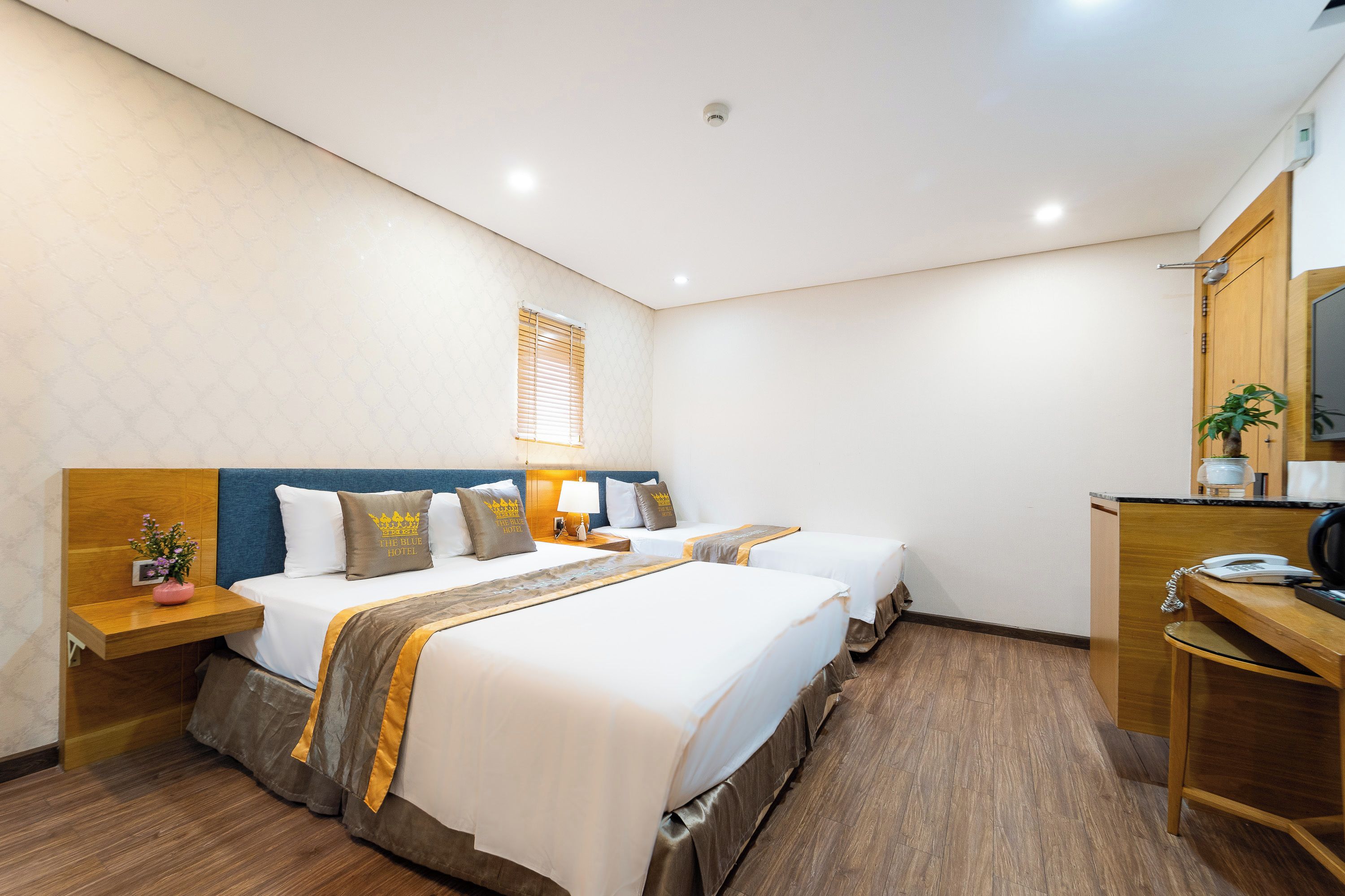 Habitació d'hotel amb dos llits, una taula de treball, un mirall i una finestra amb persianes.