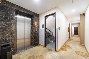 A hotel corridor with a marble wall, an elevator, a staircase, and a carpeted floor.