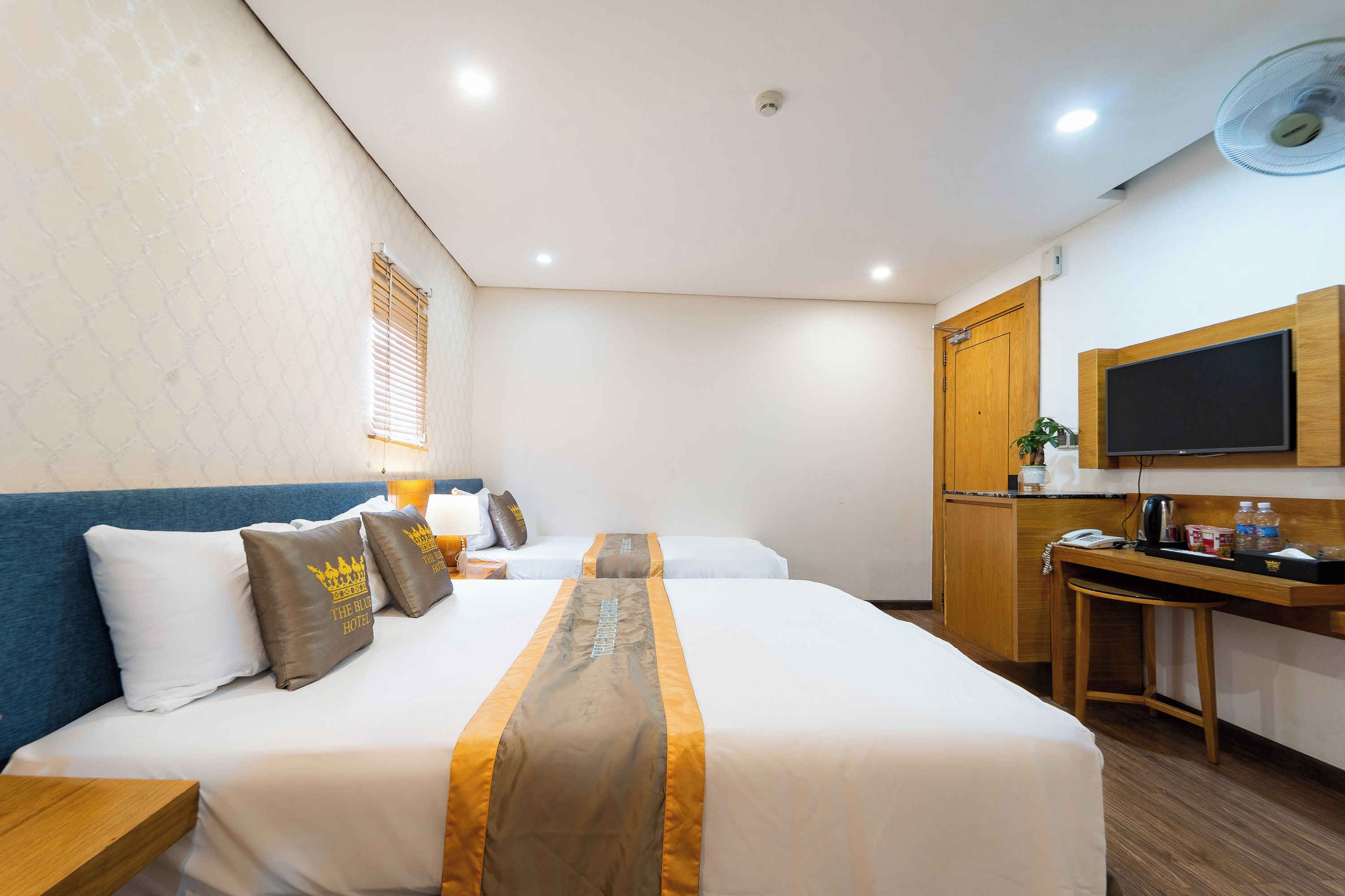 A hotel room with two beds, a desk, a television, and a window with blinds.