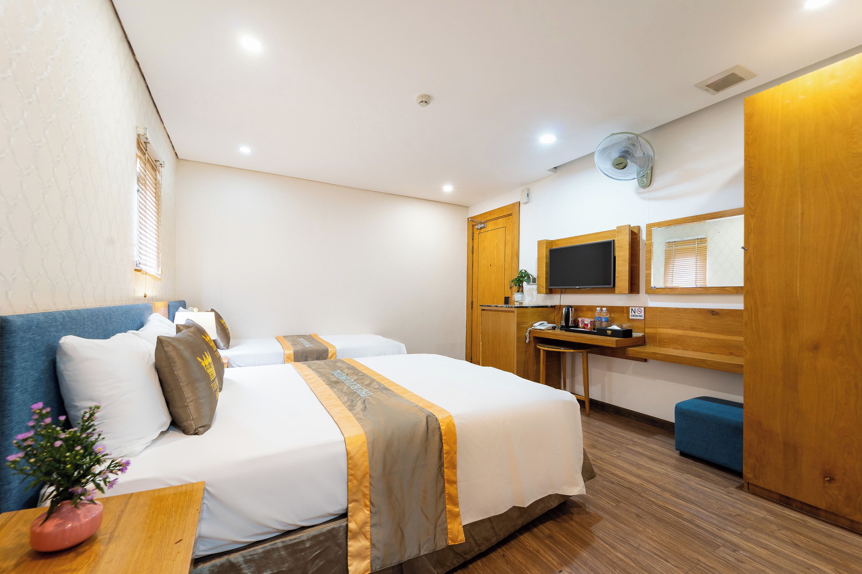 Habitación de hotel con cama, mesita de noche, un pequeño escritorio, una silla, televisor y ventana con persianas.