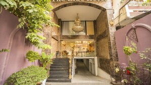 Entrada para o Blue Hotel com uma escadaria imponente, um lustre e vegetação exuberante.