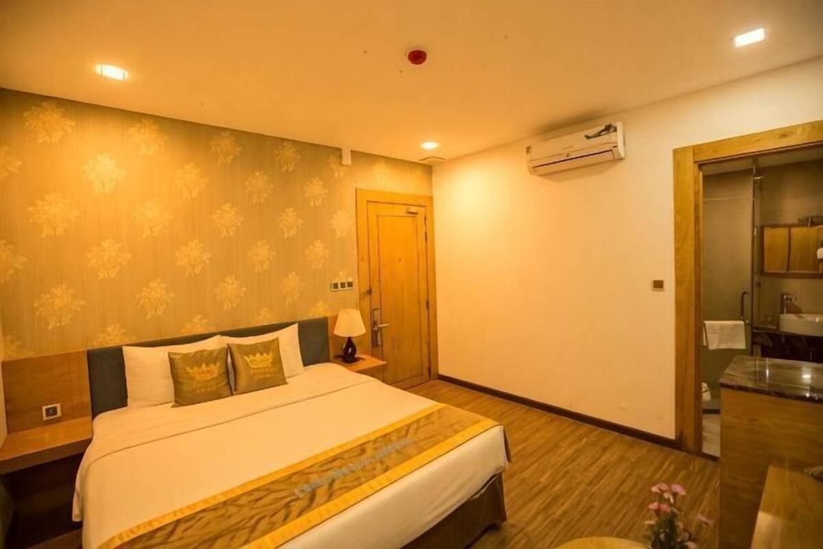 Une chambre d’hôtel avec un grand lit, une table de chevet, une commode, un appareil de climatisation, une salle de bain avec un miroir et un espace douche.