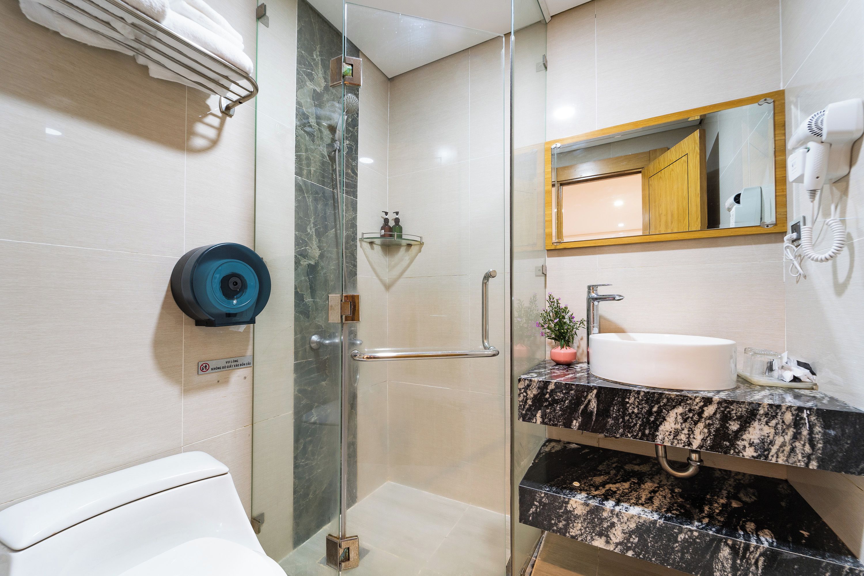 Un baño moderno con cabina de ducha de vidrio, inodoro blanco, lavabo de mármol y ducha de mano.