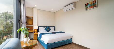 Habitación de hotel con cama, mesita de noche, planta en maceta, ventana y aire acondicionado.