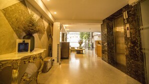 Um saguão de hotel com paredes de mármore, balcão de recepção, área de estar e elevador.