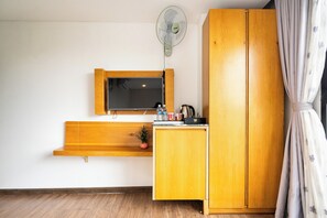 A room with a wooden cabinet, a television mounted on the wall, and a small shelf with various items.