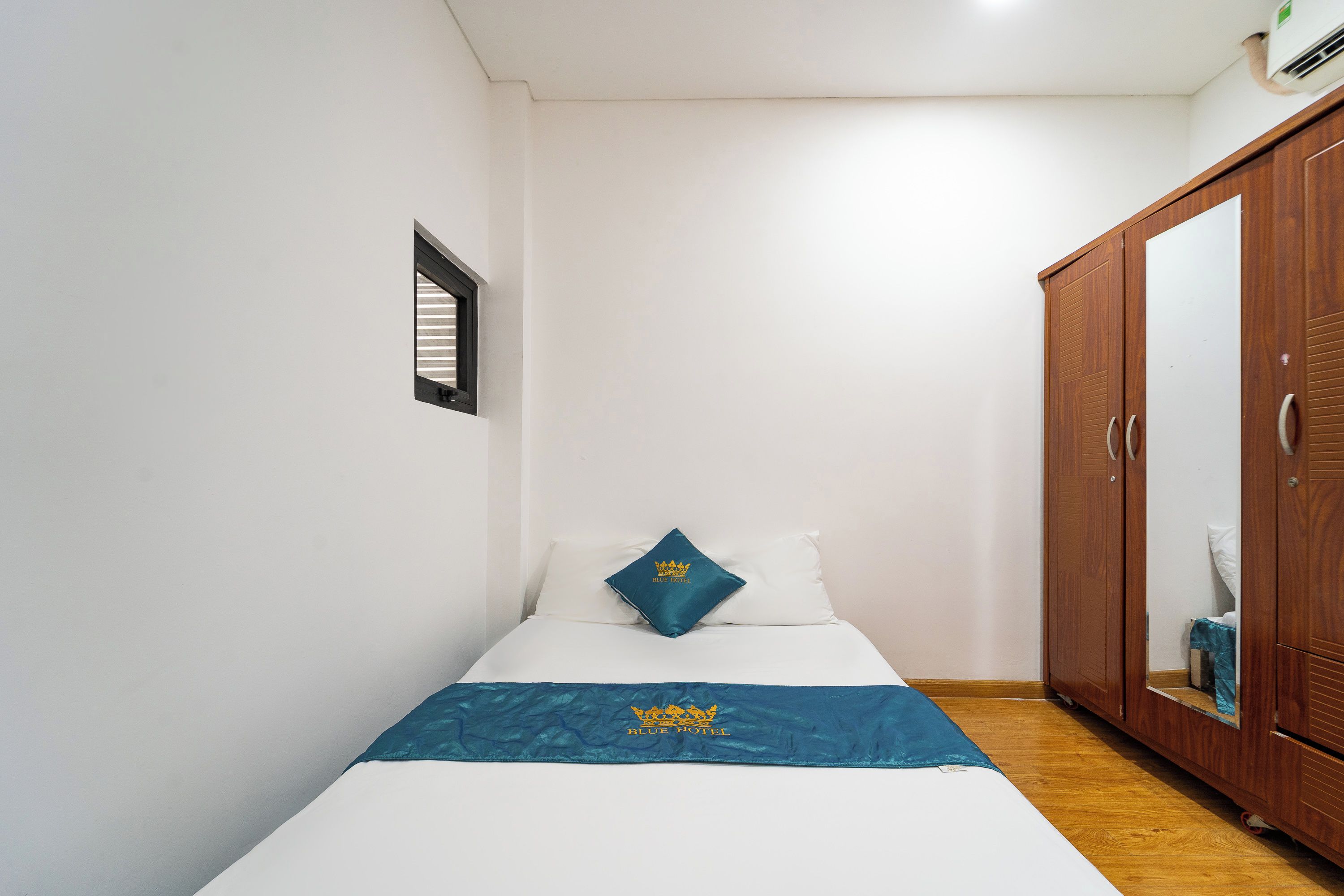 Une petite chambre avec un lit simple, une armoire en bois et une fenêtre avec des stores.