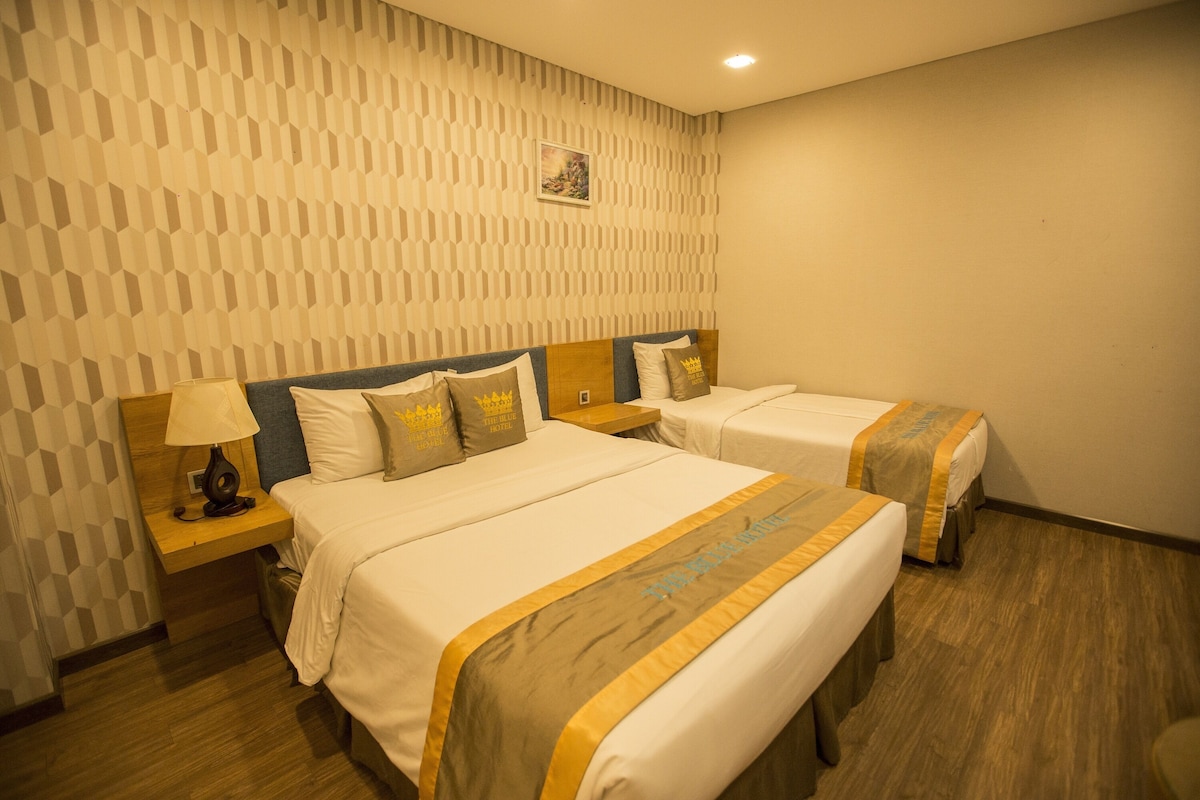 Une chambre d’hôtel avec deux lits, une tête de lit en bois, une table de chevet avec une lampe et un mur décoré d’un motif.