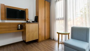Quarto de hotel moderno com televisão de tela plana fixada na parede, móveis de madeira, uma mesinha e vista através de grandes janelas.